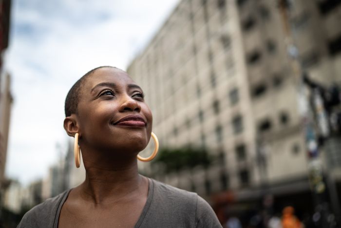 Person smiling with confidence outdoors, wearing hoop earrings and a V-neck top, with an urban background