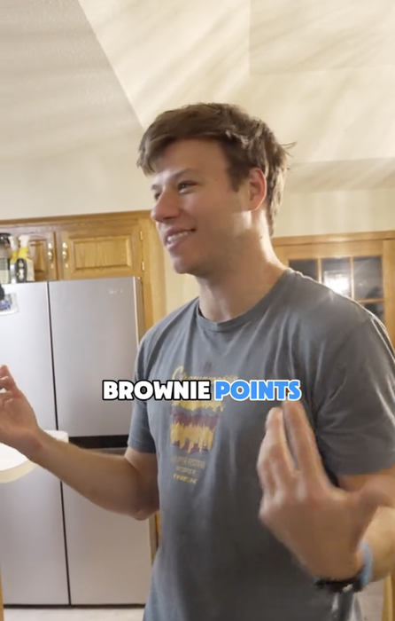 A person smiling and gesturing in a kitchen, wearing a casual t-shirt. Text overlay reads 'Brownie Points.'