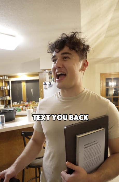 A person in a kitchen holding a book, wearing casual attire, with a text overlay that reads, 'Text you back.'
