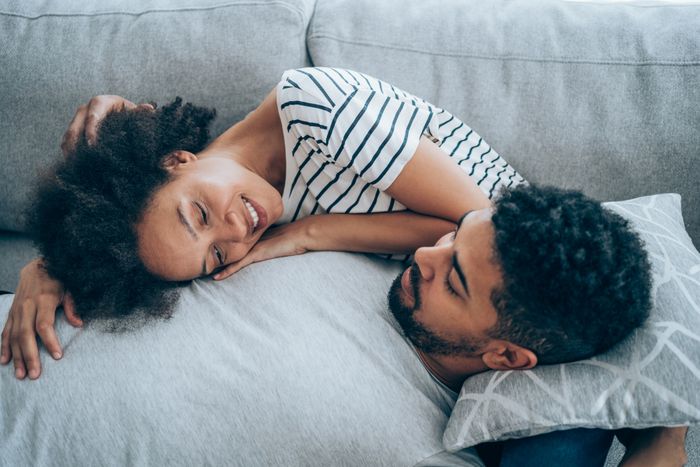 A couple relaxes together on a couch, smiling and resting their heads on pillows, conveying a sense of comfort and intimacy