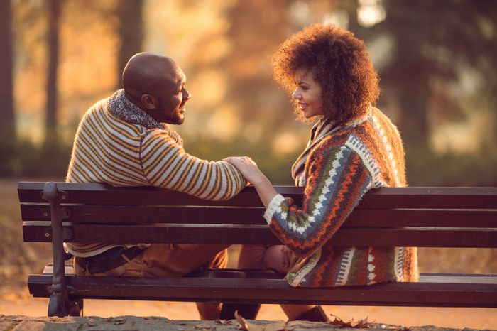 Couple sitting on a park bench, sharing a moment, bundled in cozy knit sweaters, surrounded by autumn foliage