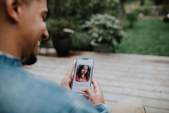 Person using a dating app on a smartphone outdoors, viewing a profile picture of a woman with long hair