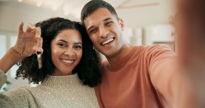 A couple smiles while holding a key inside their new home, suggesting they've just purchased a house together.