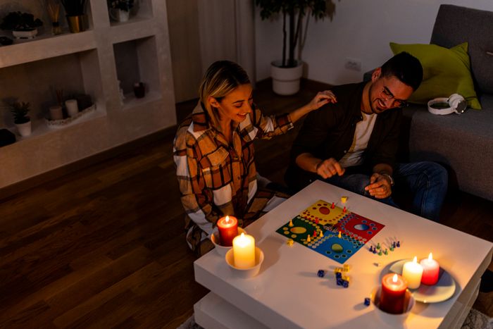 A couple plays a board game on a coffee table surrounded by lit candles, creating a cozy atmosphere in a living room