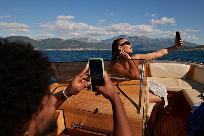 A person on a boat taking a selfie, while another captures the moment with a phone. They're enjoying the scenic view on the water, evoking feelings of romance and relaxation