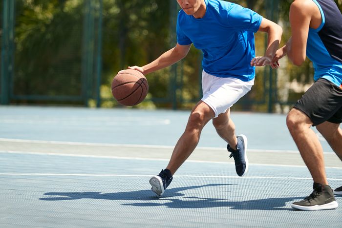 Two people playing basketball outdoors. One is dribbling the ball mid-action, while the other is defending. No celebrity or red carpet context in sight.