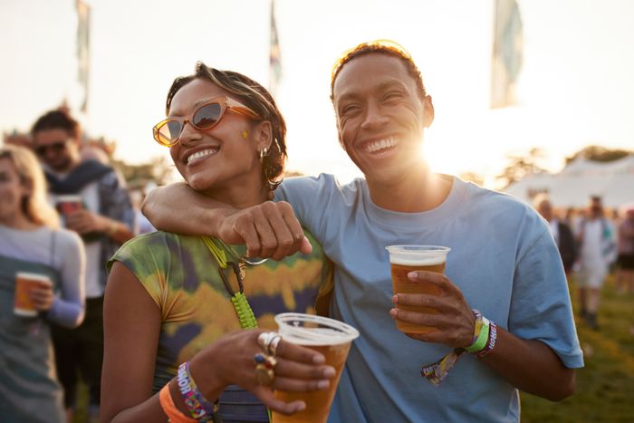 A happy couple enjoying an outdoor event, each holding a cup, with the sun setting behind them, creating a warm and joyful atmosphere