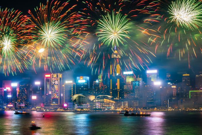 The city skyline illuminated by vibrant fireworks, reflecting off the water, creating a festive and lively atmosphere in an urban setting.
