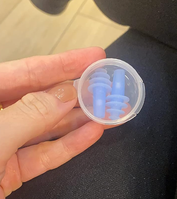 A reviewer holding a case with small blue spiraling earplugs.