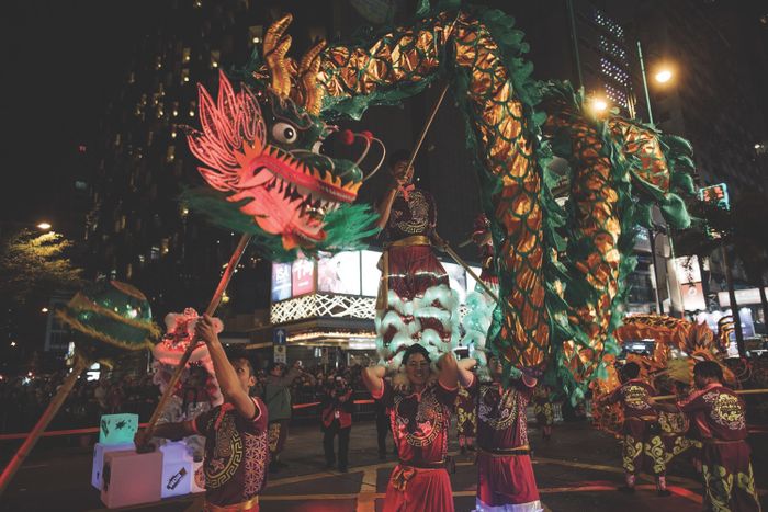 Performers skillfully handle a dragon puppet during a vibrant nighttime street parade, set against a bustling city backdrop, capturing the essence of cultural celebration.