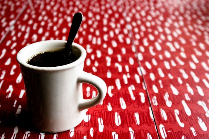 A cup of coffee with a spoon on a patterned table, evoking a cozy café atmosphere perfect for travel enthusiasts