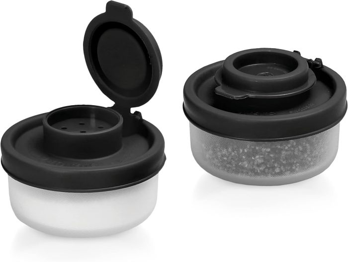 Two black plastic spice containers, one with a lid that opens to sprinkle, and the other closed, designed for convenient and compact storage in the kitchen or on-the-go.