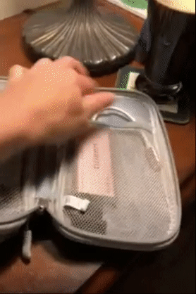 A reviewer opens a gray zippered cable organizer, revealing two compartments holding various electronics.