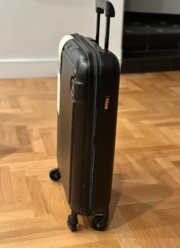 A wheeled black hard-shell suitcase with a handle placed on a parquet floor. Perfect for travel or shopping purposes.