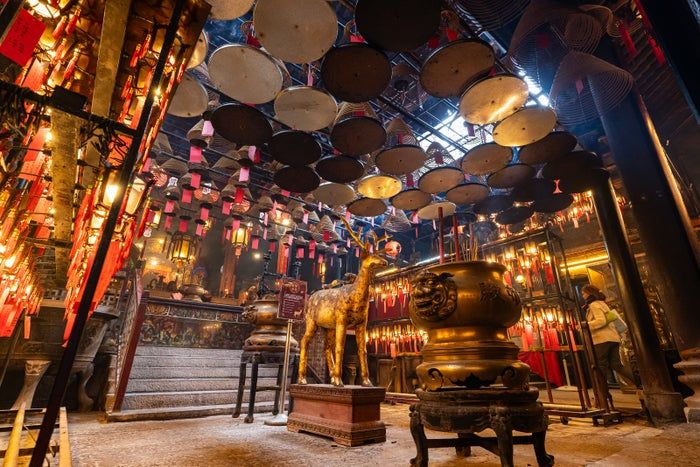 A tranquil temple setting, with large incense coils hanging from the ceiling, a brass incense burner, and glowing red lanterns creating a peaceful ambiance.