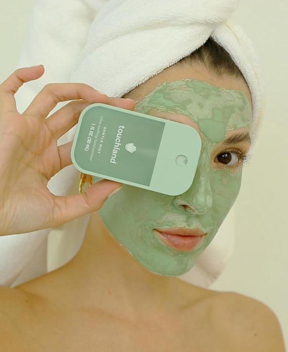 A model wearing a face mask holds a Touchland sanitizer bottle.