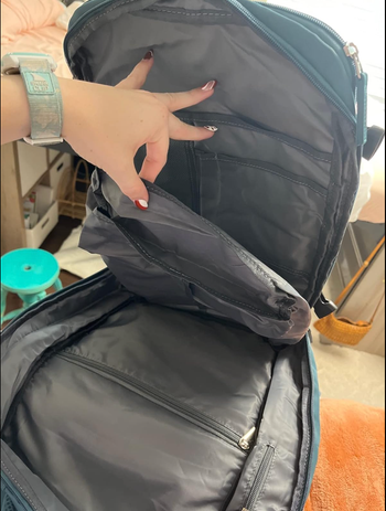 A reviewer holding the green version of the backpack open, showing off all the pockets inside.