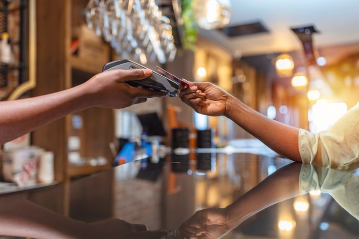 A person pays by card using a contactless terminal at a hotel reception, with bright lighting and modern decor in the background.