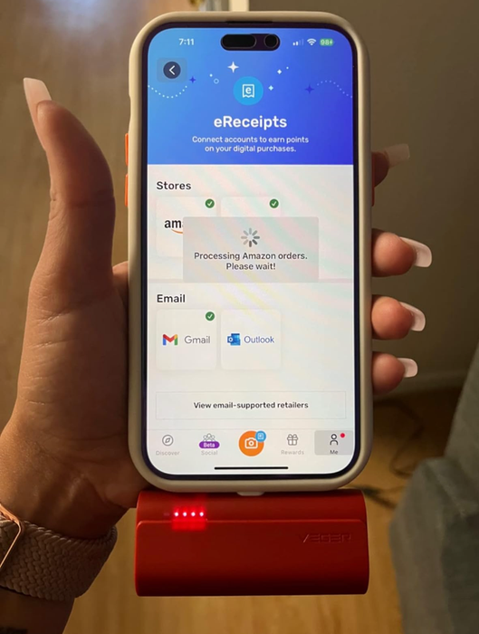 A person holding a smartphone with a small red portable charger attached to the bottom.