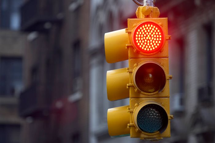 A traffic light displaying a red signal in an urban setting, instructing vehicles to stop.