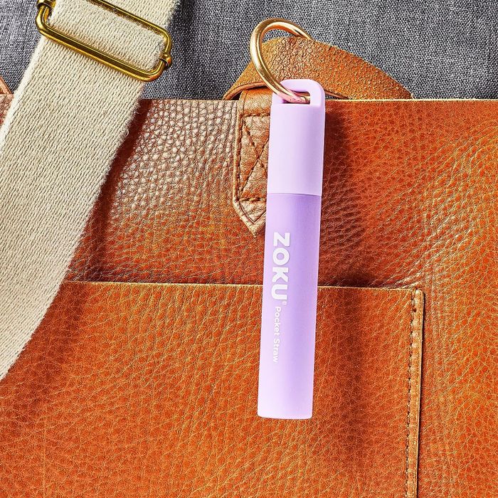 A small purple, portable straw tucked inside a case attached to a purse as a keychain.