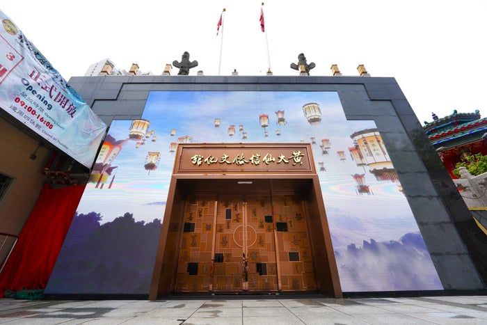 A contemporary building with a grand digital display showcasing a fantasy scene. Flags and traditional architecture adorn the roof.