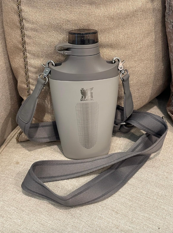 A reusable water bottle with a minimalist design and shoulder strap.