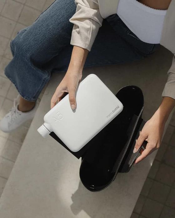 A model holding a square-shaped, flat, white matte flask-style water bottle over their laptop bag.