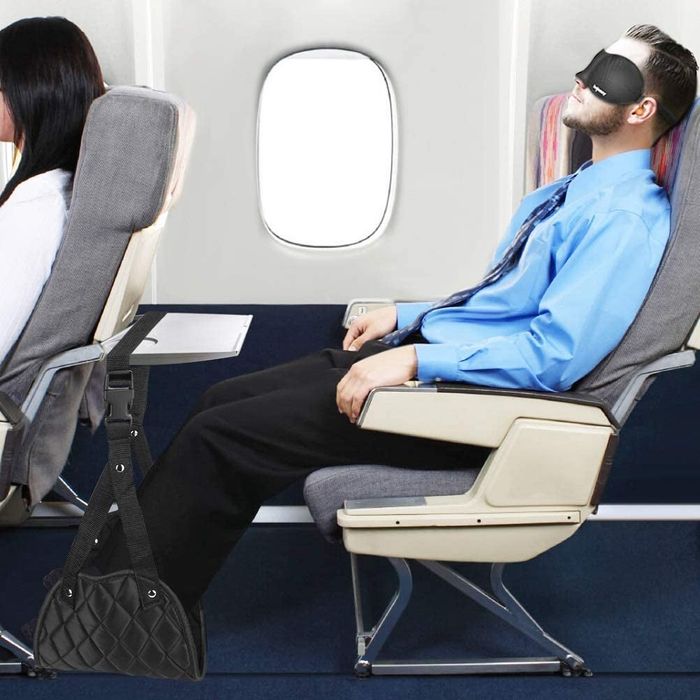 A model with their feet resting comfortably in a black hammock suspended from an airline tray table.