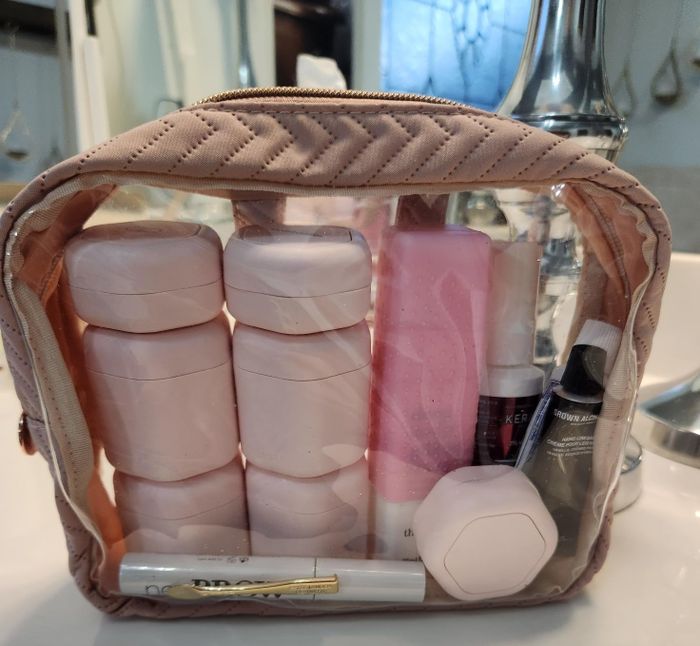 A clear travel toiletry bag with some of the pink Cadence Capsules inside.
