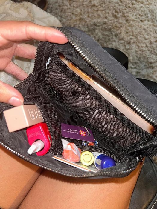 A photo from a reviewer showing the interior of their black belt bag, which holds a phone, lipstick, lip balm, and plenty of other small items.
