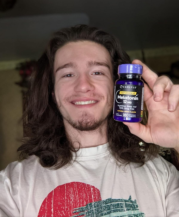 A smiling reviewer holding up a bottle of melatonin pills.