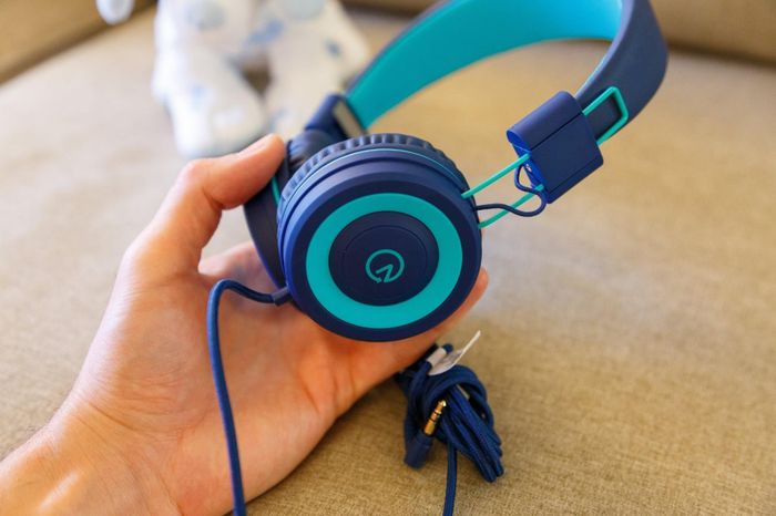 A reviewer holding a pair of navy and teal-colored kids' headphones.
