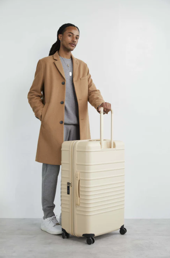 A model standing next to the white 29-inch Béis suitcase, with the handle extended.