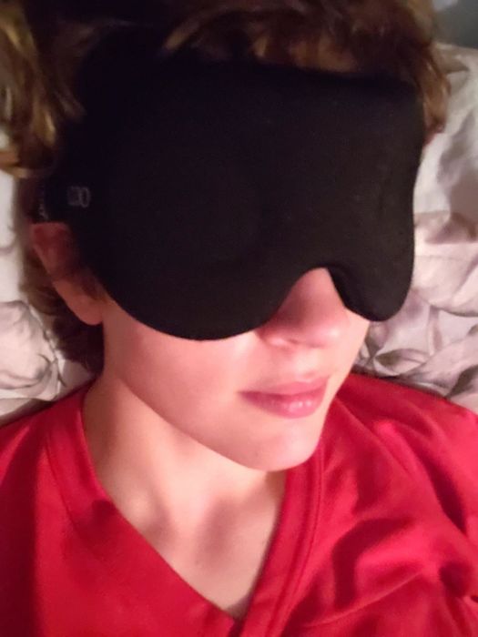 A reviewer wearing a sleek black sleep mask.