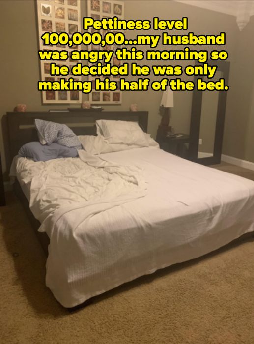 An unmade bed with white sheets sits in a bedroom, adorned with artwork above and a floor mirror beside a nightstand with a lamp.
