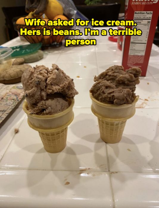 Two ice cream cones with scoops placed on a white countertop, surrounded by kitchen items and a cereal box in the background