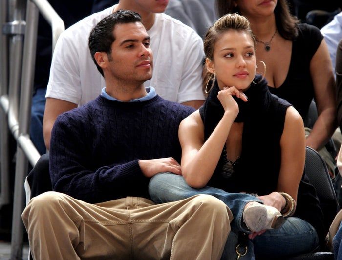 At an event, the couple sits together. The woman, dressed in a sleeveless top and jeans, appears thoughtful, while the man, dressed in a sweater and khakis, looks at ease.