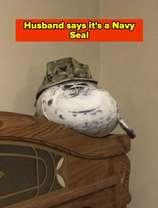 A plush seal toy sporting a military-style hat, placed on a wooden headboard in a bedroom