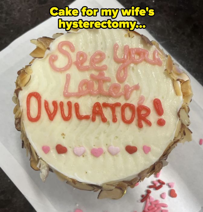 A round cake with the phrase 'See You Later, Ovulator!' written on top, adorned with heart-shaped sprinkles and almond slices along the sides