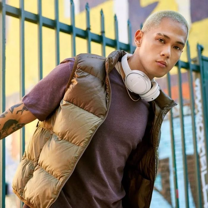 Person sporting a shiny puffer vest, t-shirt, and white headphones around their neck, striking a stylish pose against an urban backdrop