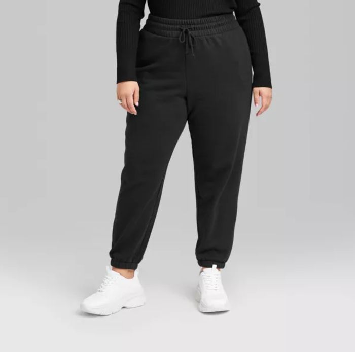A person dressed in casual black jogger pants, long-sleeve shirt, and white sneakers