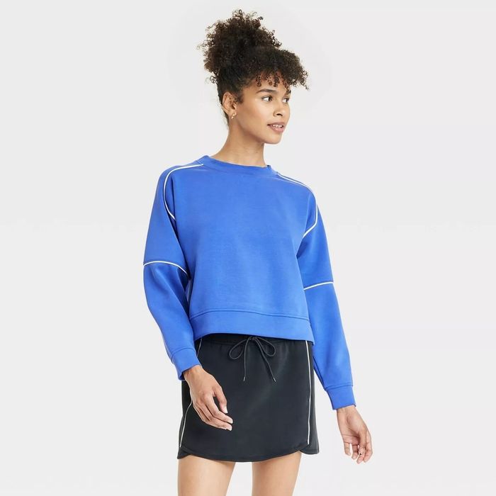 A model wearing a relaxed, long-sleeve blue sweatshirt paired with a black skirt