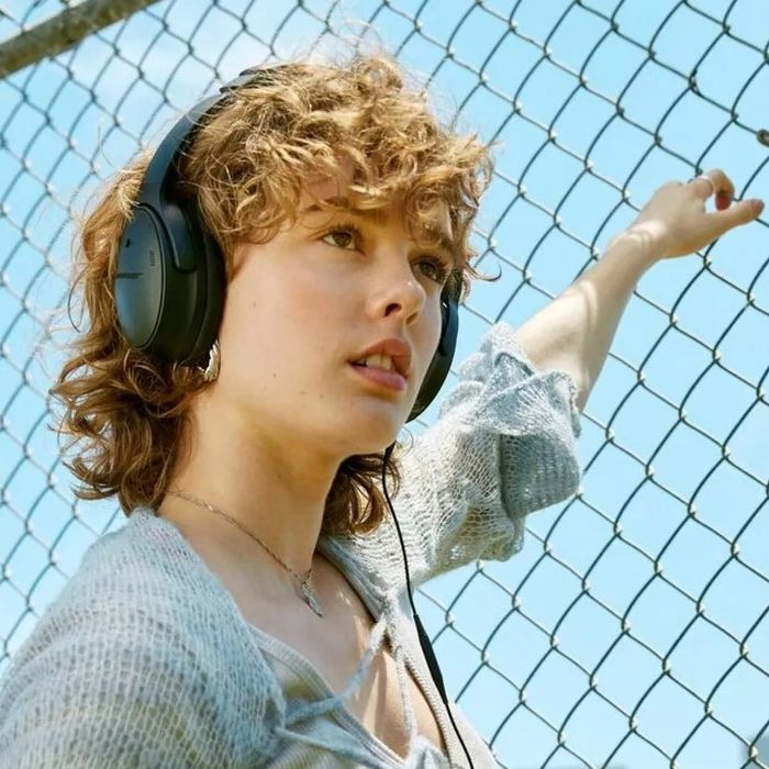 Person wearing wireless headphones, leaning against a chain-link fence, gazing upwards