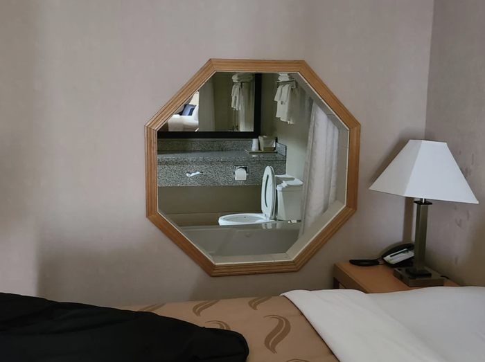 A hotel room with a bathroom window that offers a direct view of the toilet from the bed