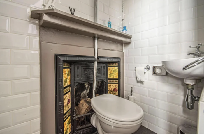 A bathroom featuring a decorative fireplace behind a toilet and a wall-mounted sink