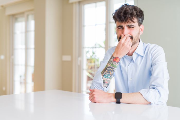 A man covering his nose, trying to avoid a bad smell.