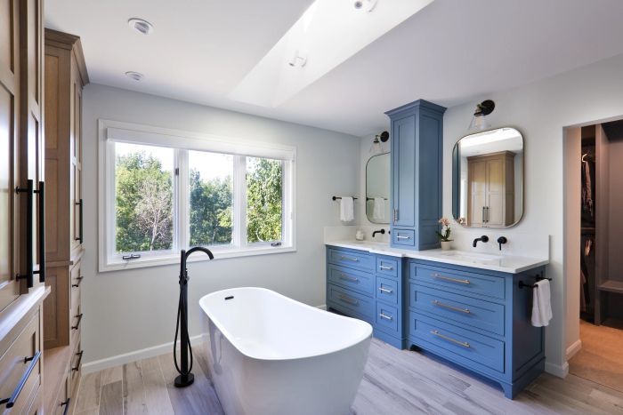 A contemporary bathroom featuring a freestanding bathtub, sleek blue vanity cabinets, and a spacious mirror.