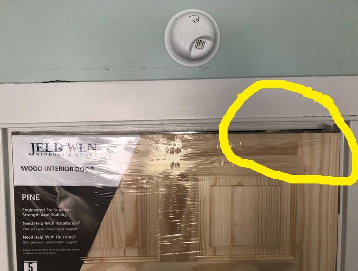 A new wooden door with protective plastic covering that doesn’t fit