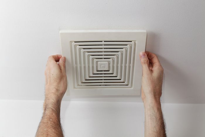 A person making adjustments to a bathroom vent.